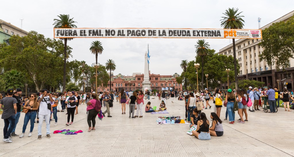 Plaza de Mayo, vaste esplanade où des gens assis attendent le début de la marche avec leurs pancartes