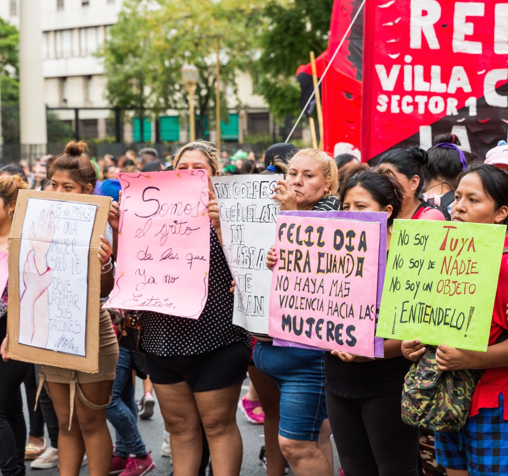 Cinq femmes d'âges divers alignées portent des pancartes.