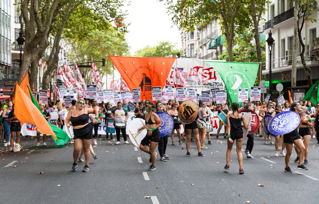 Des manifestantes habillés de shorts noirs et de top noirs dansent dans le cortège de la manifestation, elles portent des boucliers. 